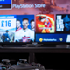 A Playstation 4 controller on a table in front of a TV showing offerings on Playstation Store